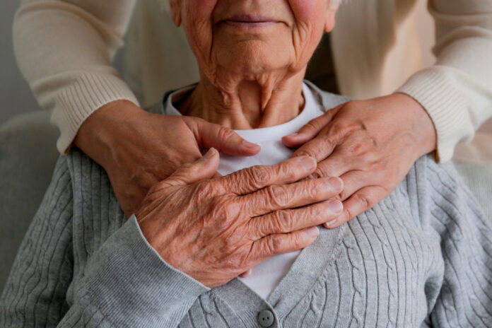 Unrecognizable female expressing care towards an elderly lady, hugging her from behind holding hands. Two adult women of different age. Family values concept. lose up, copy space, background.